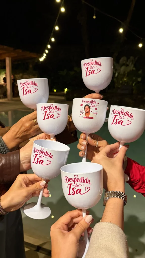 Convidadas erguem taças personalizadas da despedida de solteira de Isabella Arantes durante um brinde.