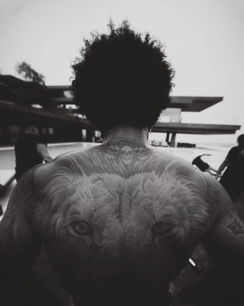 Memphis Depay é fotografado de costas, exibindo tatuagens nas costas e no pescoço, próximo à área da piscina de uma mansão, em imagem em preto e branco. 