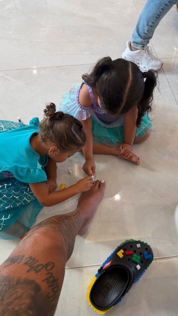 Mavie e Antonella pintam as unhas dos pés de Neymar enquanto as duas crianças, vestidas de princesa Ariel, brincam ao lado do jogador durante as férias nos Estados Unidos.