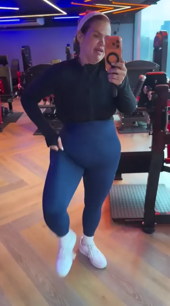 Após perder mais de 100 kg, Thais Carla revela que roupas de academia não servem mais 2 Selfie média e desfocada da influenciadora Thais Carla, de rosto sério, em uma academia, vestindo sua jaqueta de treino preta.