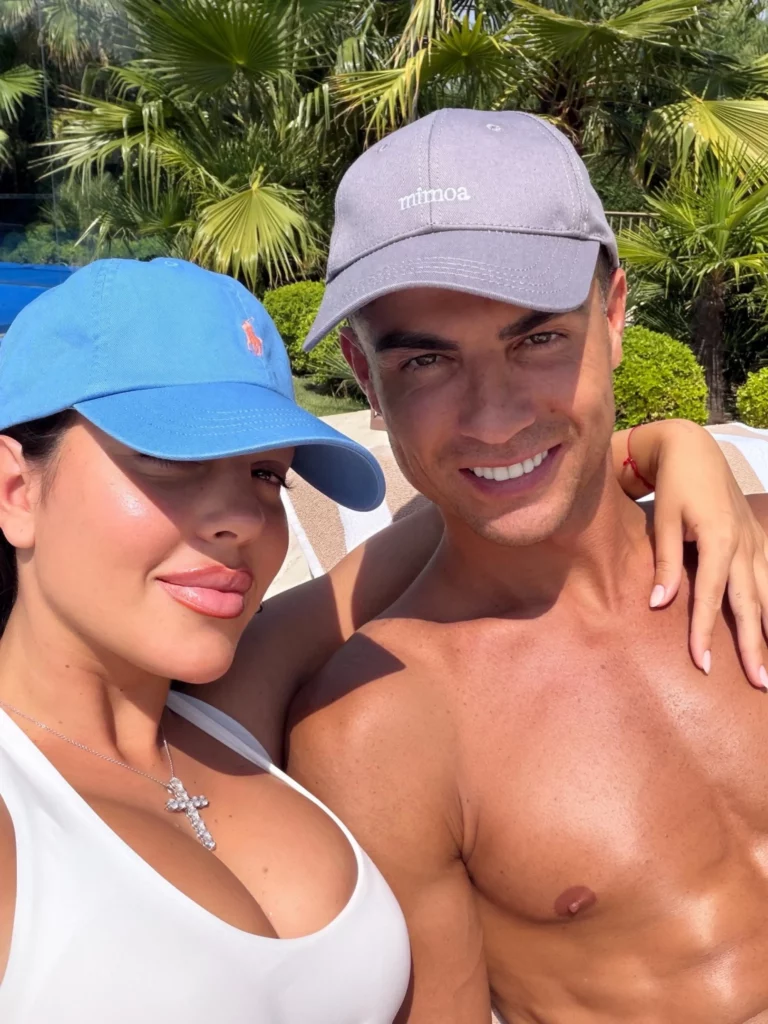 Cristiano Ronaldo e Georgina Rodríguez sorrindo juntos sob o sol, usando bonés de beisebol.
