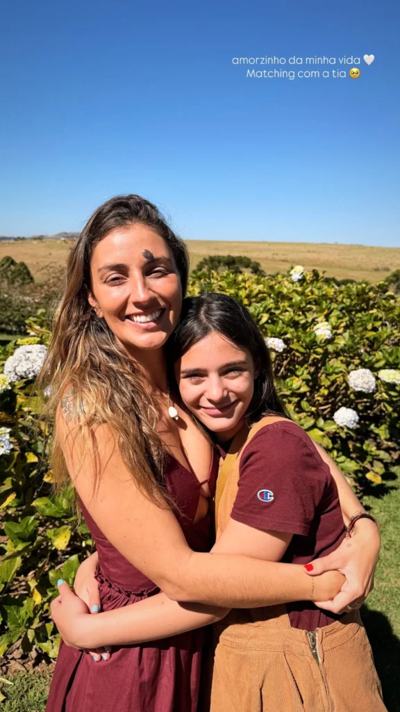 Nina Forlin abraça uma jovem em área externa cercada por jardins durante o fim de semana em Campos do Jordão.