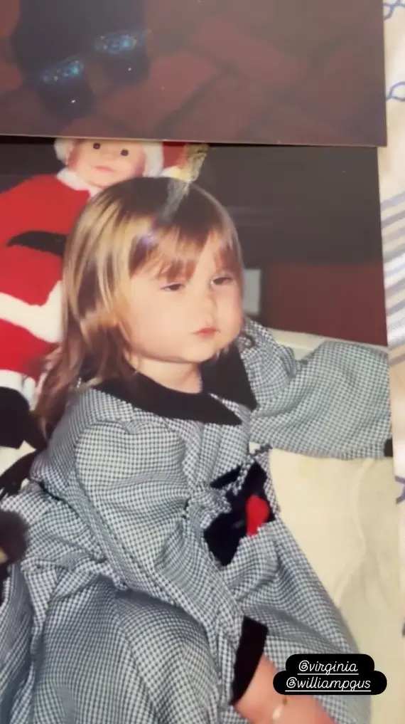 Virginia criança com vestido xadrez e laço vermelho; ao fundo, um boneco de Papai Noel.