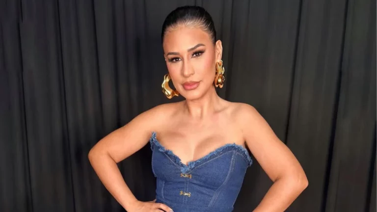 Simone Mendes posa para foto usando vestido jeans tomara que caia e brincos dourados, diante de um fundo preto.