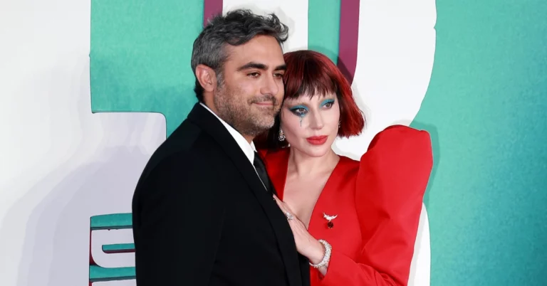 Lady Gaga posa ao lado de Michael Polansky em evento, usando vestido vermelho e maquiagem azul nos olhos