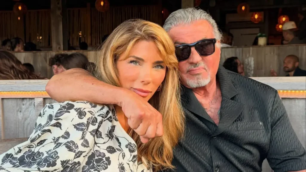Sylvester Stallone e Jennifer Flavin posam juntos em um restaurante, abraçados e sorrindo para a câmera.