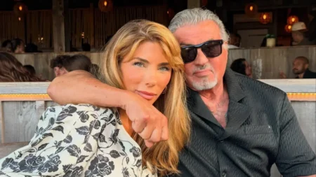 Sylvester Stallone e Jennifer Flavin posam juntos em um restaurante, abraçados e sorrindo para a câmera.