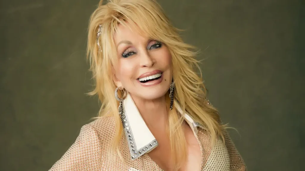 Dolly Parton sorri para a câmera em retrato com figurino dourado, acessórios brilhantes e cabelos loiros soltos.