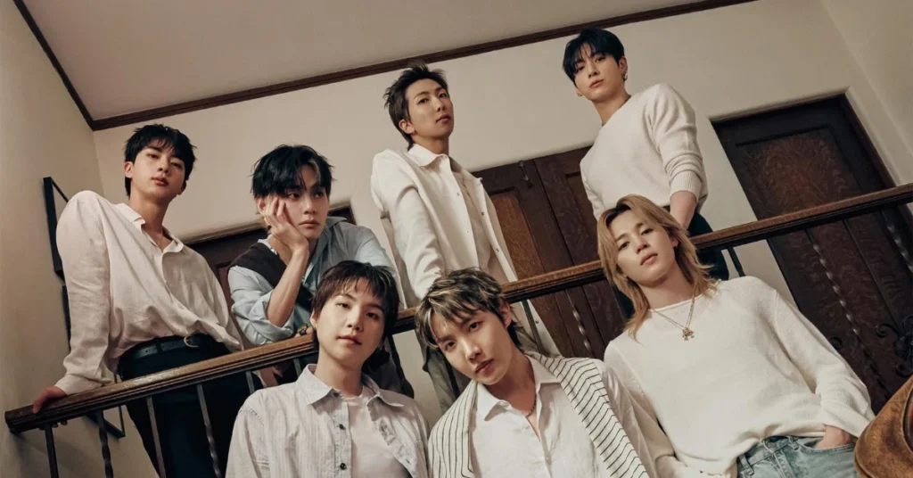 RM, do BTS, desabafa sobre fãs na porta dos hotéis: ‘Ninguém consegue dormir bem’ Sete integrantes do BTS posam em uma escadaria interna, com roupas em tons claros, apoiados ou próximos a um corrimão de madeira