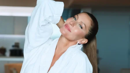 Gisele Bündchen posa com roupão branco, cabelo preso em rabo de cavalo e maquiagem leve.