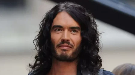 Russell Brand aparece em retrato com cabelos longos e escuros, barba e expressão séria.