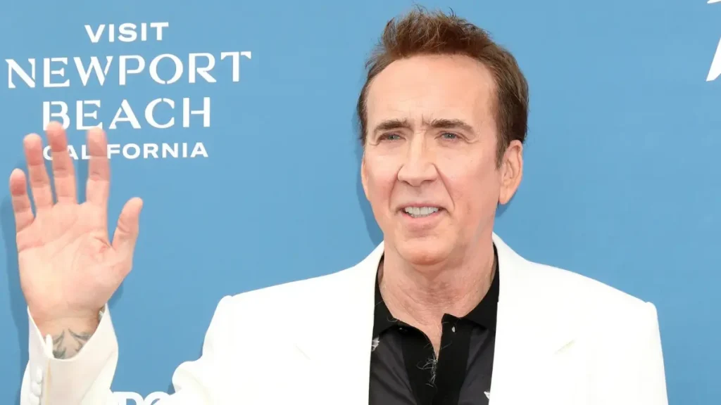 Nicolas Cage posa com blazer branco e camisa preta durante evento.