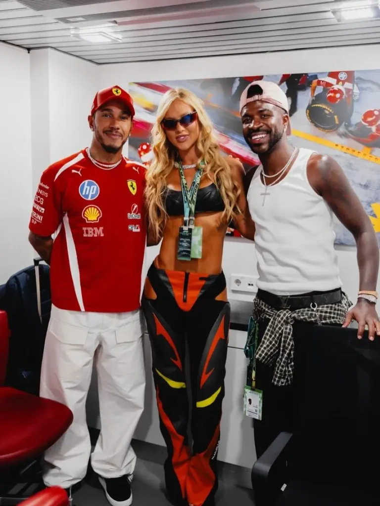 Virginia Fonseca aparece entre Lewis Hamilton, à esquerda, com uniforme vermelho da Ferrari, e Vini Jr., à direita, de camiseta branca, durante encontro nos bastidores do Grande Prêmio da Espanha de Fórmula 1.